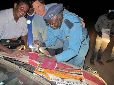 Driver Philip Young watches as a Sudanese official stamps his passport on the shores of Lake Nasser at the Sudan Egypt border.