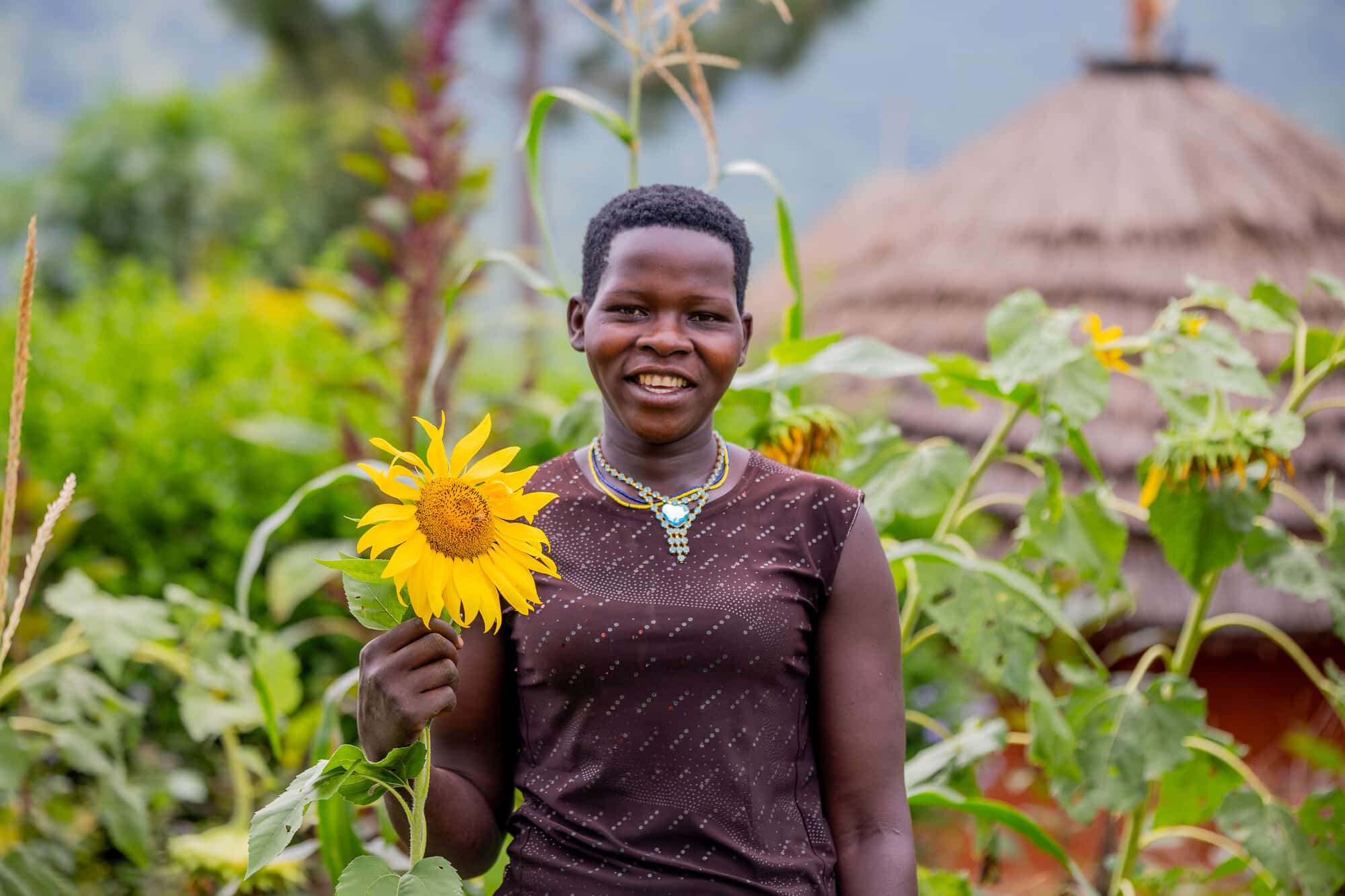 Annette, a smallholder farmer pictured with a sunflower in Karamoja, Uganda.