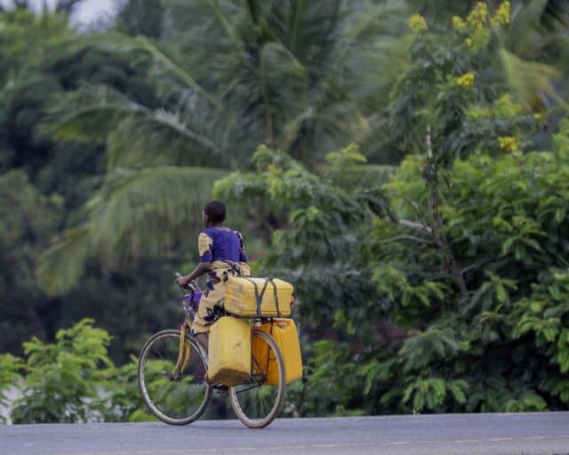 Person on a bike carrying tubs, in Tanzania.