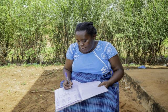 Female farmer Damaris, sat outside updating her account book.