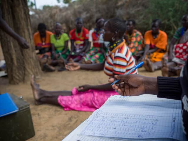 Women seated in a Village Saving and Loan Association meeting, finance book in the foreground.