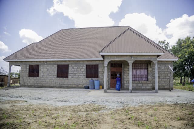 Tanzanian farmer Teluvina stood outside her newly built house.