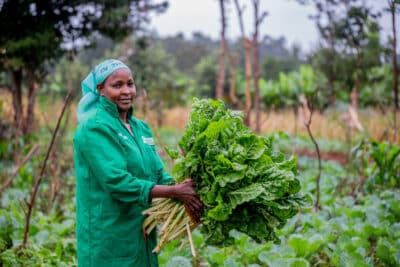 Perpetua Pius holding vegetables grown on her farm using regenerative farming methods in Embu County, Kenya.