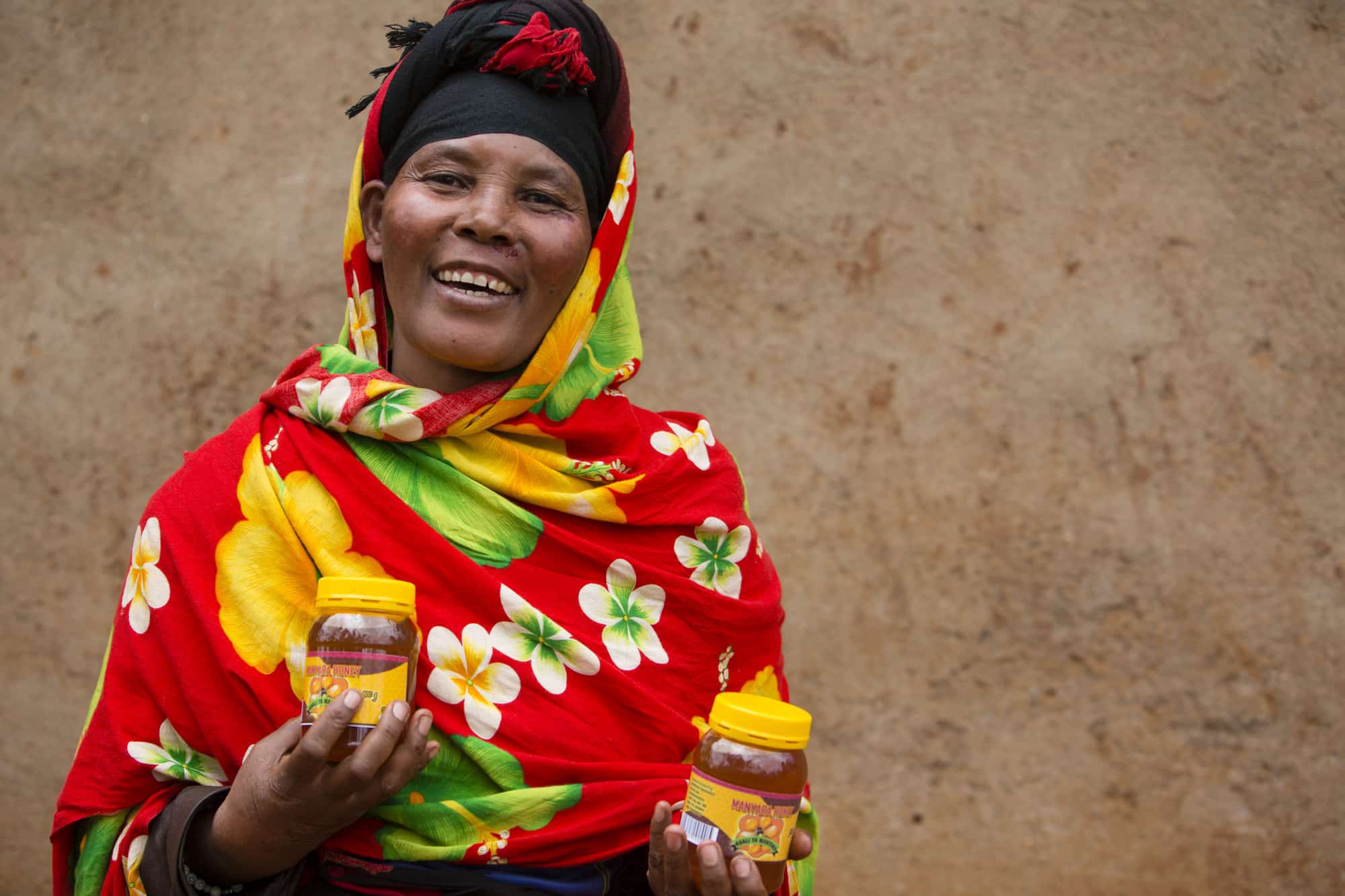 Regina, a beekeeper from Babati in Tanzania holding jars of honey.
