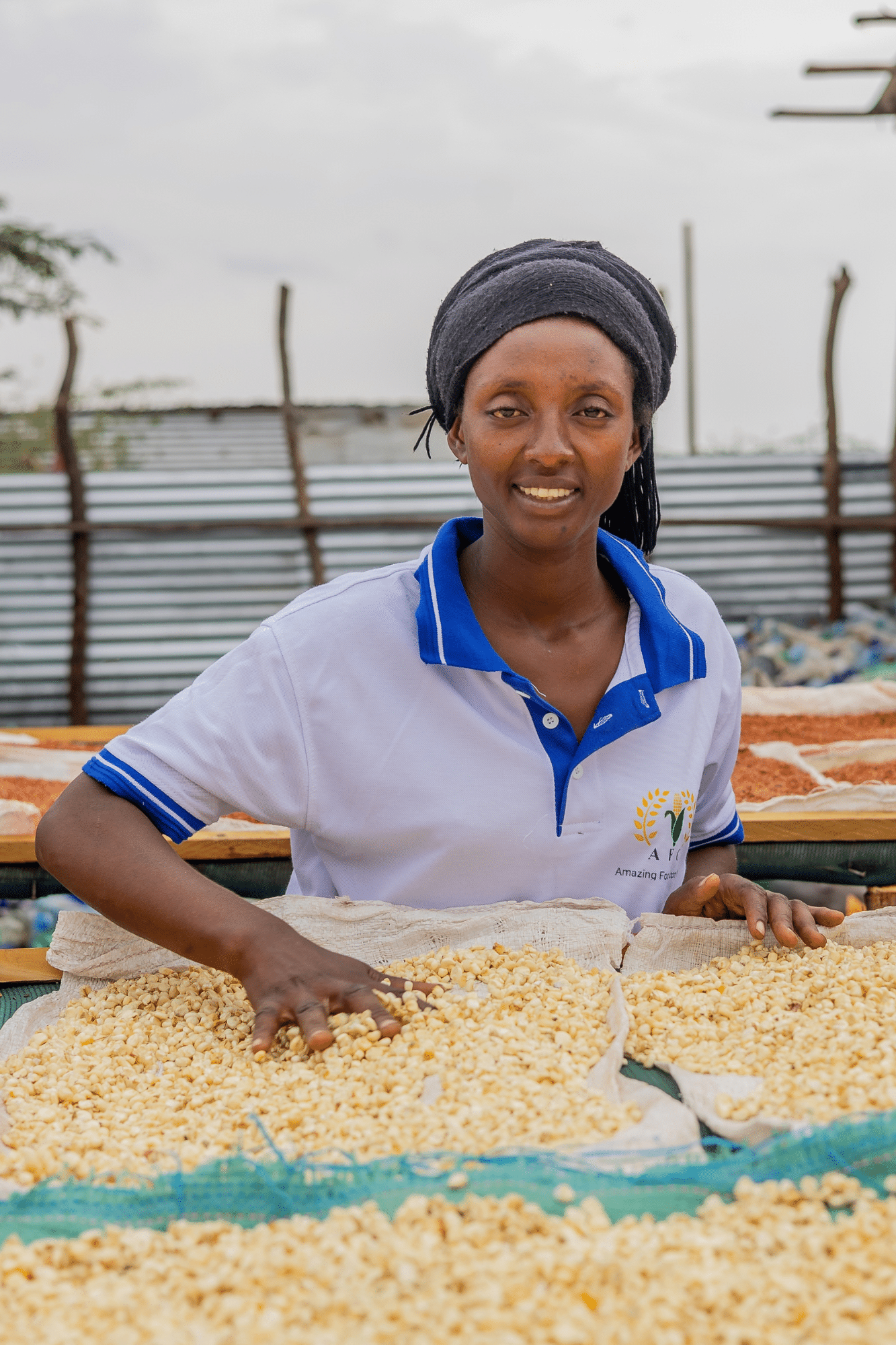 Fabiola Nzoyikorera at her flour milling shop in Kakuma, the photo shows her smiling at the camera whilst running her fingers through some grains.