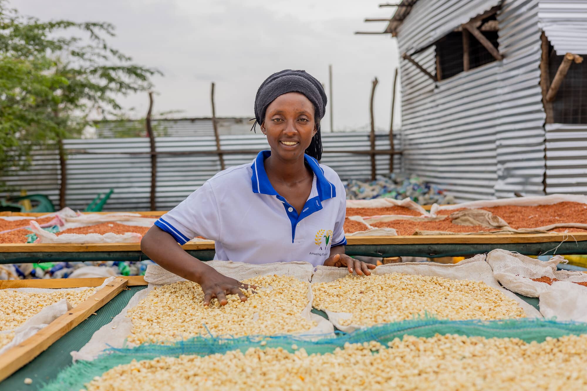Fabiola Nzoyikorera at her flour milling shop in Kakuma, the photo shows her smiling at the camera whilst running her fingers through some grains.